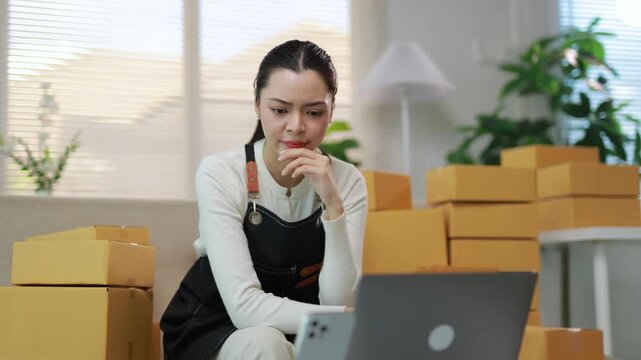 Stressed small business owner feeling tired while working on her laptop with packages for shipping in the background