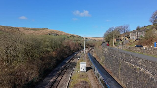 Low down Drone footage of  Blue commuter train heading towards Standedge Tunnel in the village of Marsden, West Yorkshire