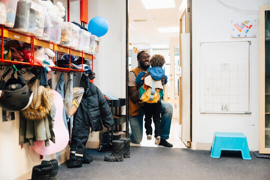 Happy male teacher holding boy in arms while kneeling on classroom floor