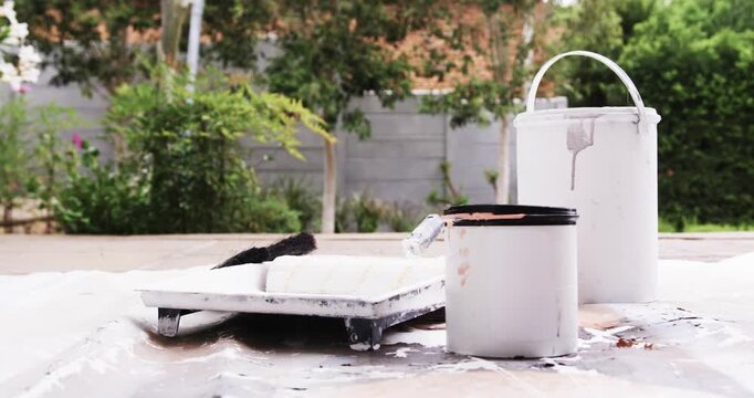 Small dark bird landing on paint roller, perching, preening on tray near paint cans in backyard