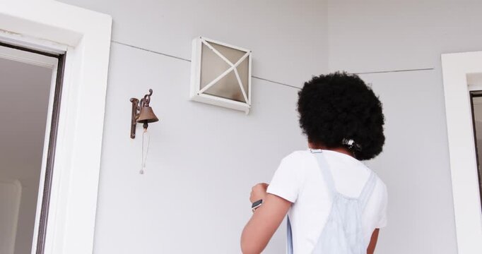 Female standing back to camera at porch, noticing bell cord, reaching and ringing brass bell
