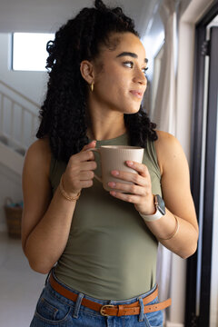 Woman standing near sliding glass door, holding ribbed ceramic mug and gazing at sunlight