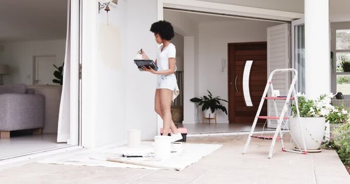 Woman starting by applying brush holding tray on porch wall, stepping on stool, preparing pass