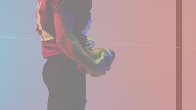 Camera pulling back, football player cradling ball and helmet on blue pink set for sports promo