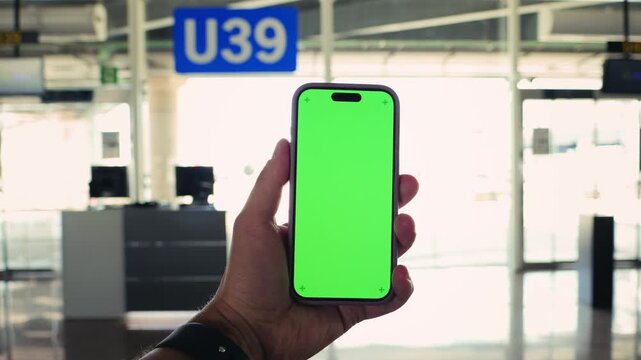 In the airport terminal, close-up of a tourist's hand with a phone, green screen against the background of the exit from the airport terminal, holding a mobile phone against the background of a green 