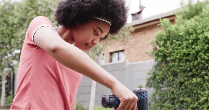 African American woman in pink tee aligning drill over mark, drilling plank in backyard for DIY