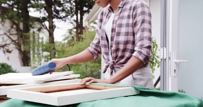 African American woman picking stapler stapling smoothing securing green cloth onto frames on patio