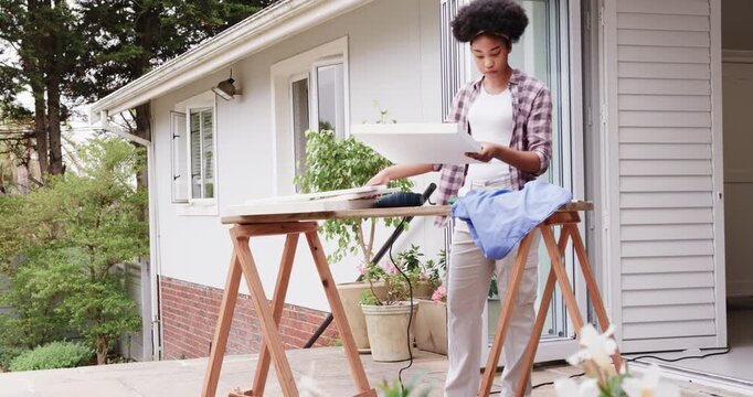 African American woman lifting panel on sawhorses on porch, checking fit for assembly, copy space