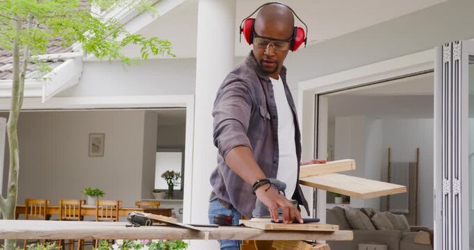 Man checking boards then sanding on patio with orbital sander, with earmuffs smoothing wood