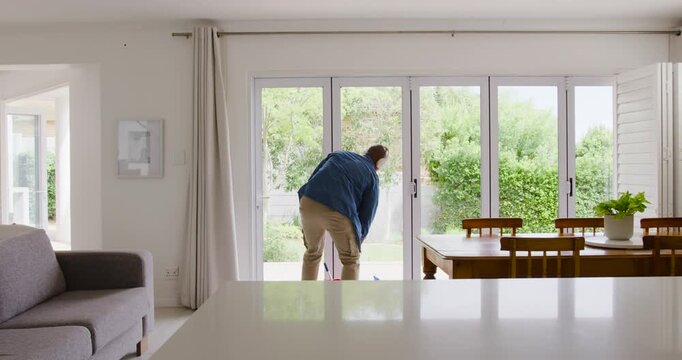Adult man at home noticing item, bending at glass doors and probing track with weeder retrieving