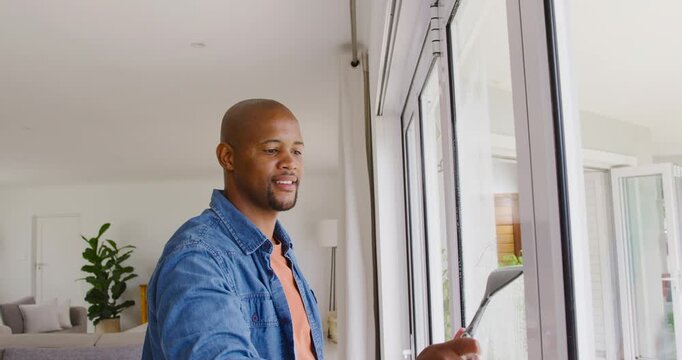 Man is spraying cleaner and is pulling rubber squeegee at sliding glass doors to remove streaks