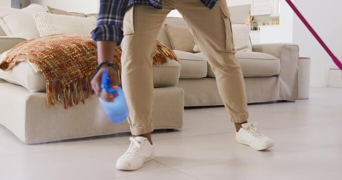 African American man preparing blue spray bottle, mopping tile floor with pink mop for cleaning