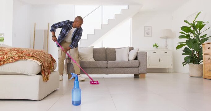 African American man holding pink mop cleaning tiled floor at home for deep cleaning
