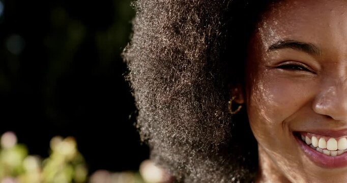African American woman smiling widening grin in garden as sunlight falling, hair, gold hoop showing