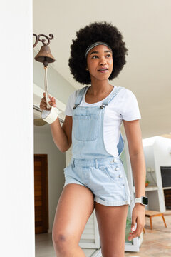 African American woman pulling metal bell rope on porch, wearing denim overalls and smartwatch