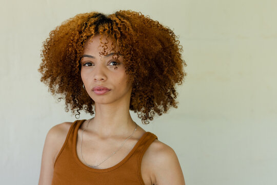 African American woman posing in studio wearing rust tank top, silver chain and hoop earrings