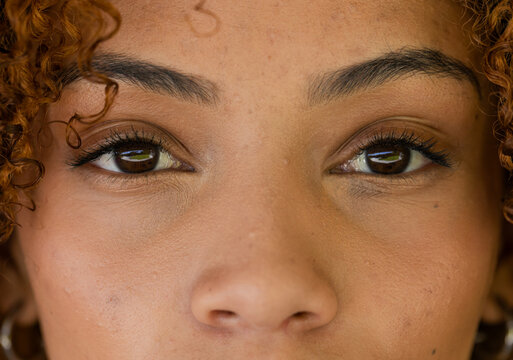 African American woman gazing into window reflections in studio, revealing curly hair hoop earring