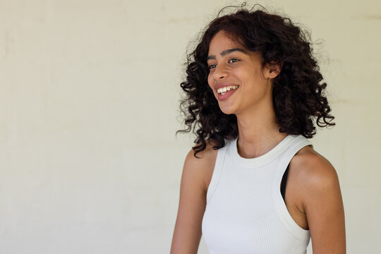African American woman smiling, turning head against plain wall wearing white tank top, copy space
