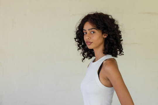African American woman posing at studio against textured wall in white tank top, copy space