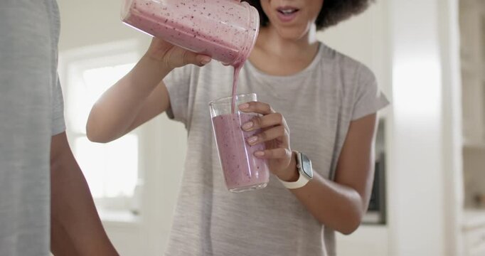 African American couple getting smoothie as woman tipping jar pouring into glass for man in kitchen