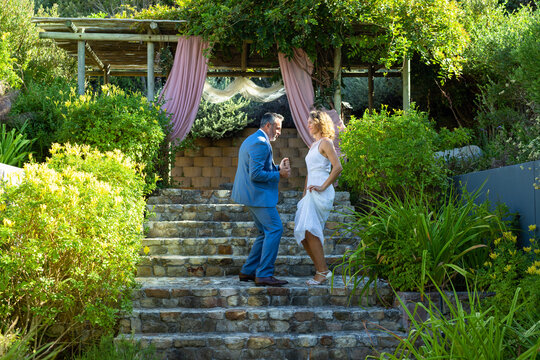 Vertical video: Couple dancing on stone steps with music starting, wedding pergola drapery glowing