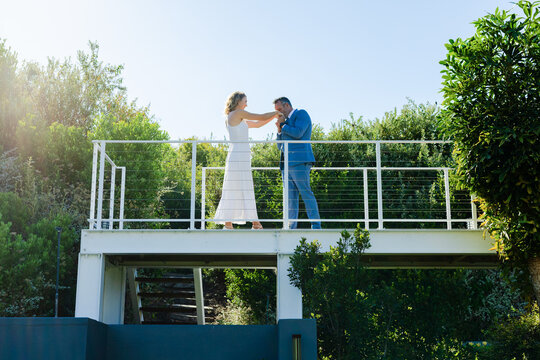 African American couple on balcony woman reaching man leaning kissing hand in formal wear in love