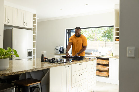 Mid adult African man wearing orange T-shirt cooking on cooktop with frying pan at granite island