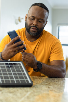 African American man testing smartphone cable with small solar panel in kitchen on granite counter