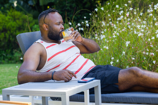 Padded lounge chair is resting on grassy lawn with glass holding citrus wedge on side table