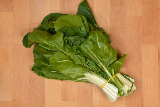 A fresh bunch of Swiss chard with large green leaves and white stalks tied with a rubber band on a light wooden surface