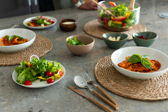 Diverse friends serving salad and sharing ravioli on stone countertop with woven placemats