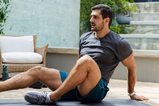 Man exercising on dark mat on paved patio wearing gray shirt shorts wristwatch green bottle nearby