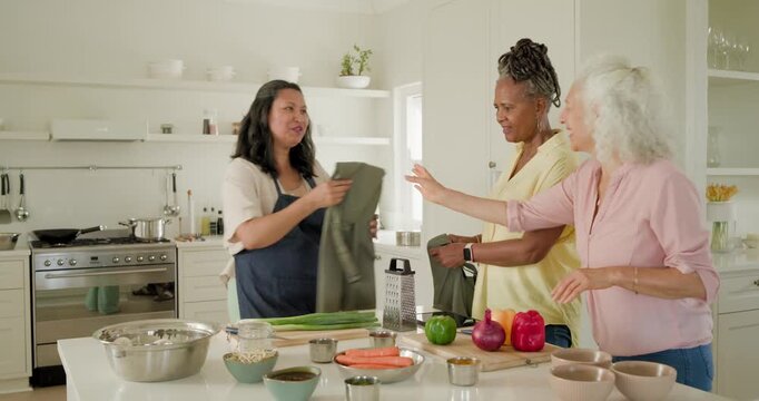 Diverse women, host handing green aprons, slipping on and tying straps at kitchen island to cook