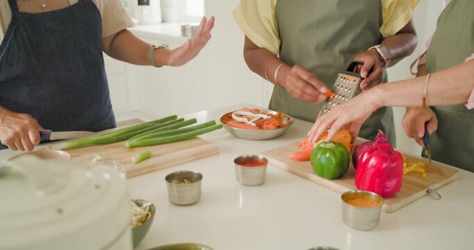 Diverse women prepping meal at kitchen island chopping peppers, grating carrot, opening rice cooker