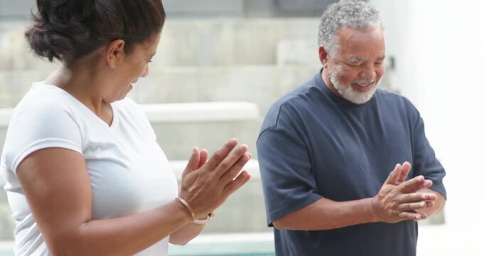 Couple standing on green yoga mat at poolside clapping then bringing hands to chest marking end