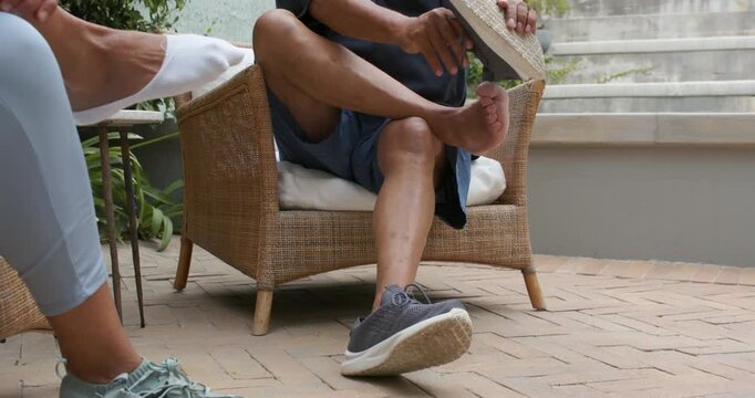 African American couple sitting on brick patio, man removing sneaker after feeling foot discomfort