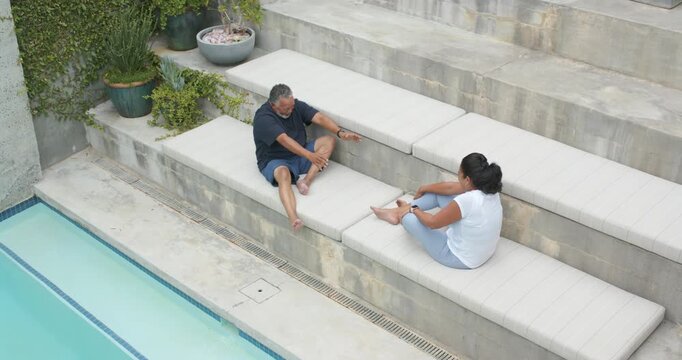 African American couple sitting on tier cushions poolside, man leaning initiating hand reaching
