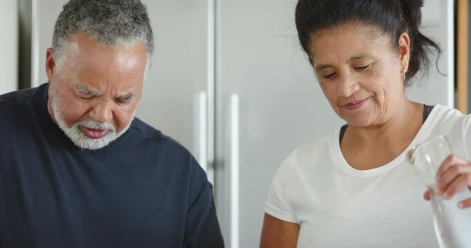 African American senior couple working at kitchen counter, woman pouring from pitcher into blender