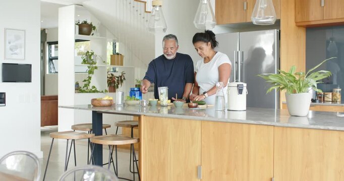 African American mature couple in navy and white wanting smoothie, preparing using blender cup