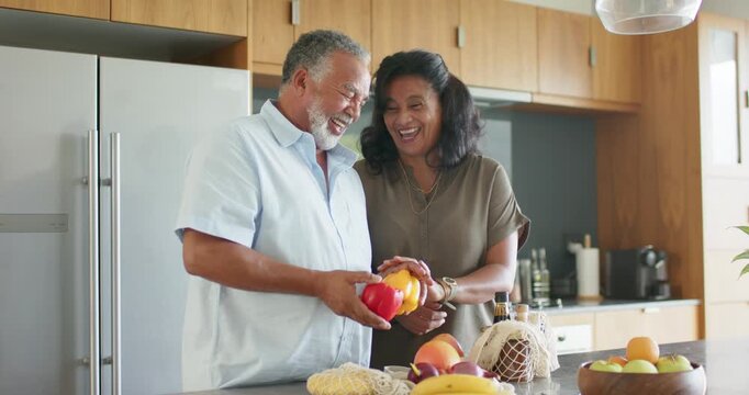 African American couple in kitchen comparing peppers after man offering red pepper for cooking