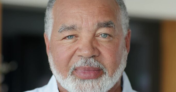 On camera senior African American man softening smile, showing beard and collared shirt