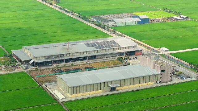 Rice Processing Facility with Solar Roof Surrounded by Paddy Fields Aerial Malaysia. Illustrating food production infrastructure, agricultural industry, distributed energy systems in Southeast Asia.