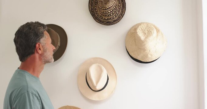 Man in his 40s spotting hat wall, inspecting pale brimmed hat, lifting, trying on, checking fit