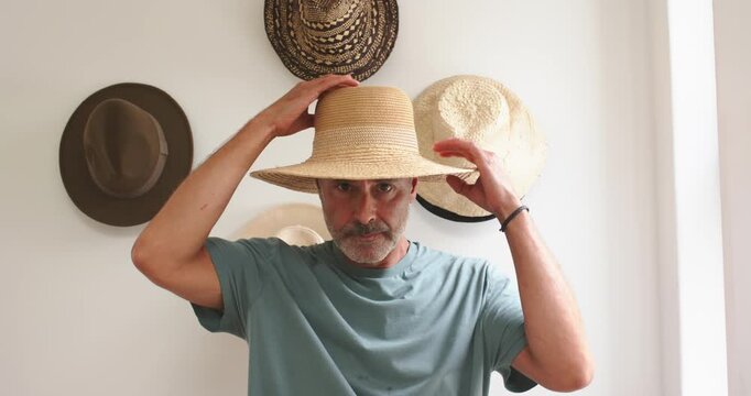 Looking down, mature man lifting wide-brim straw hat, positioning and adjusting it at home