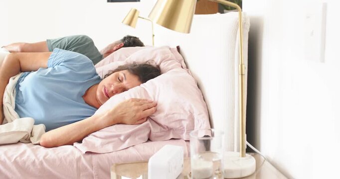 Senior couple, woman waking to light in bedroom, pressing white speaker and touching glass of water