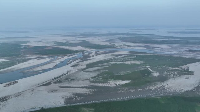Aerial view of the vast brahmaputra river delta showcasing its intricate braided channels, sandbars, and lush green islands under a hazy sky in northern india
