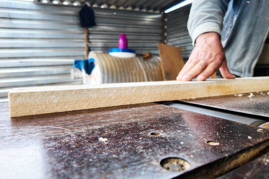 Close-Up of Carpenter Using a Jointer Planer Machine. A professional woodworker processes a pine plank on an industrial surface planer. This shot captures manual labor, craftsmanship