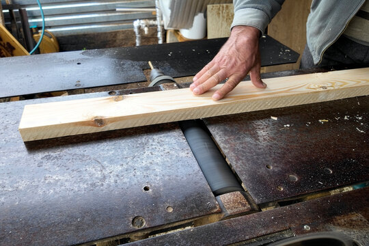 Close-Up of Carpenter Using a Jointer Planer Machine. A professional woodworker processes a pine plank on an industrial surface planer. This shot captures manual labor, craftsmanship