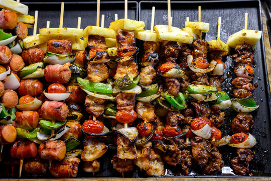 delicious grilled bbq skewers with pork chicken bacon sausage and vegetables on a black tray at a street food market