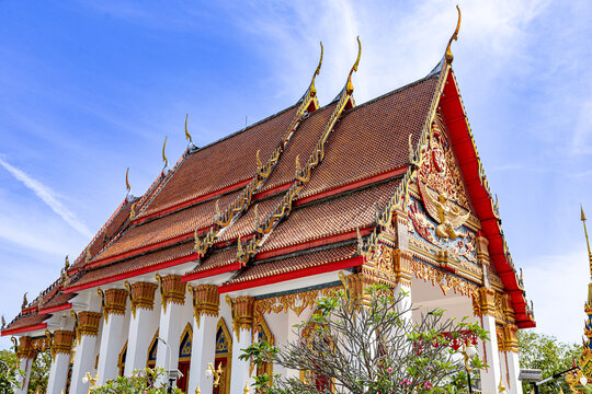 Ornate Thai Buddhist temple exterior with gilded carvings, layered red rooflines, white pillars and decorative gables. Cultural heritage, serenity and historic craftsmanship in Thailand.